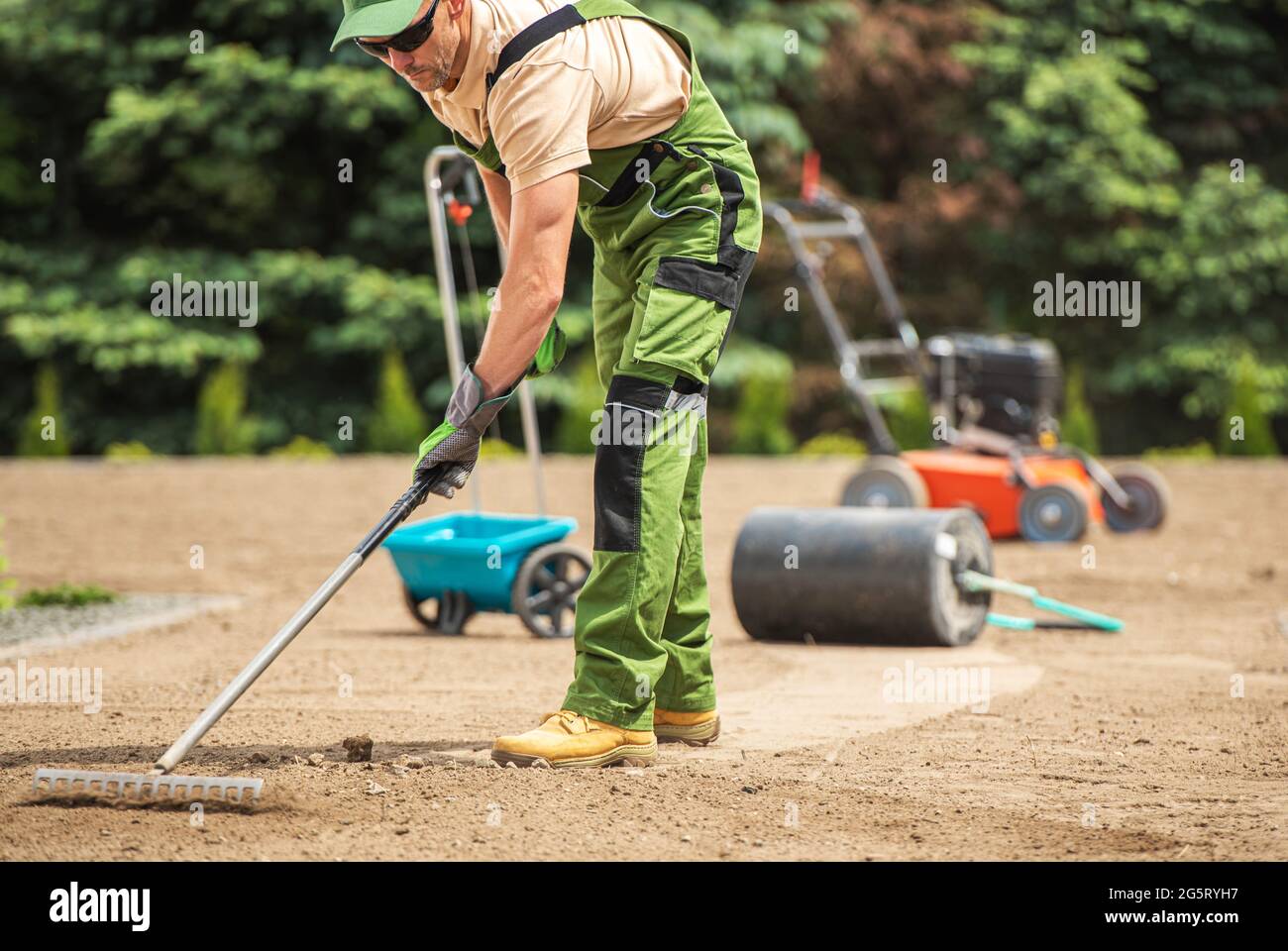 Jardinier caucasien effectuant le semis d'herbe et la préparation du sol de jardin à l'aide de râteau. Banque D'Images