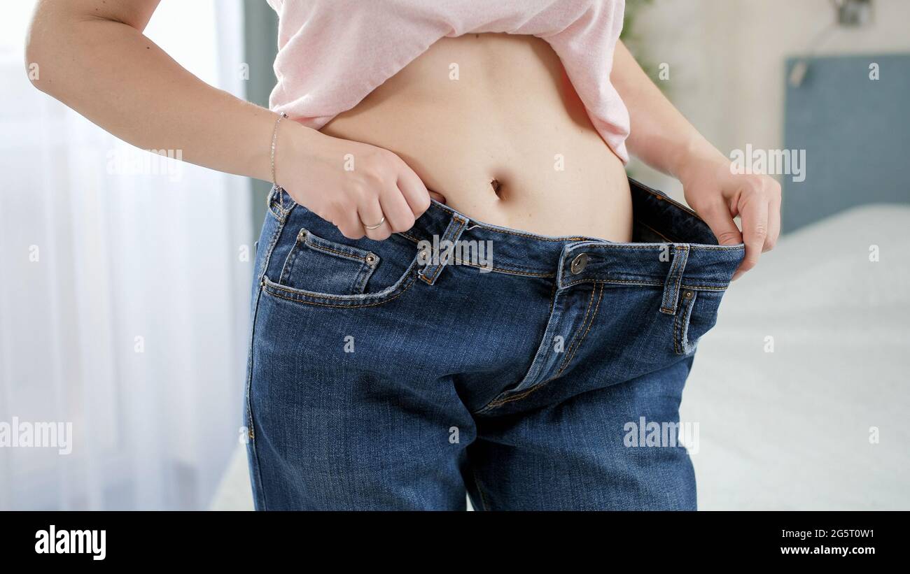 Belle jeune femme a ventre plat posant devant le miroir portant vieux grands jeans. Concept de regime de perte de poids et de mode de vie sain Photo Stock Alamy