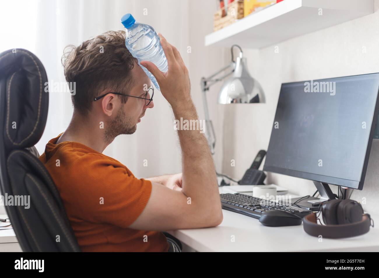 Un homme travaillant à la maison souffrant de chaleur et de soif se rafraîchit avec une bouteille d'eau à la chaude journée d'été Banque D'Images