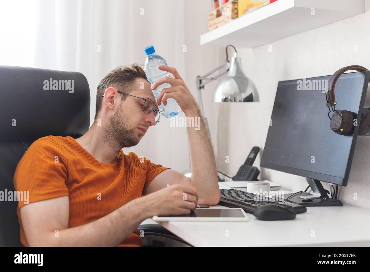 Un homme travaillant à la maison souffrant de chaleur et de soif se rafraîchit avec une bouteille d'eau à la chaude journée d'été Banque D'Images
