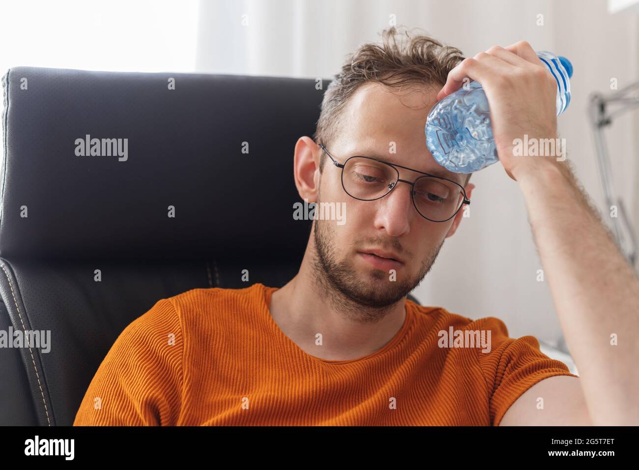 Un homme travaillant à la maison souffrant de chaleur et de soif se rafraîchit avec une bouteille d'eau à la chaude journée d'été Banque D'Images
