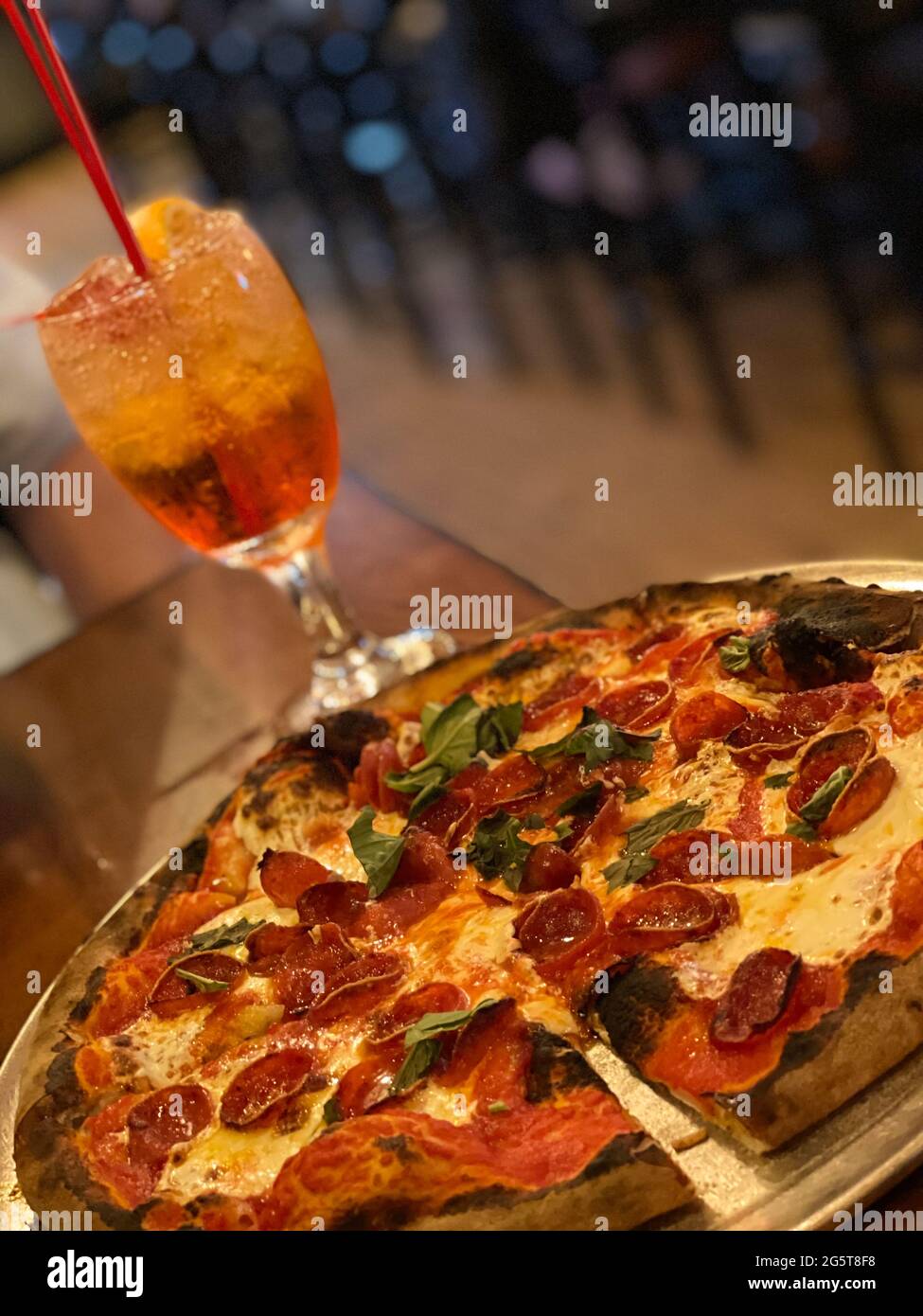 Gros plan d'une pizza au pepperoni fraîchement cuite avec des feuilles de basilic servie avec un cocktail coloré sur une table en bois dans un cadre de restaurant Banque D'Images
