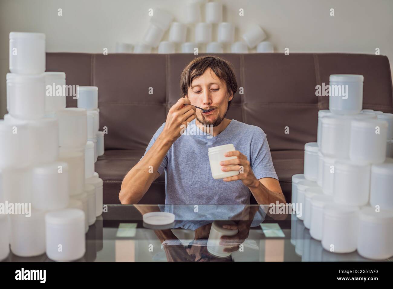 L'homme mange du yaourt et est entouré de nombreux bocaux de yaourt qu'il utilise en une année. Une énorme quantité de pots de nourriture en plastique. Consommation excessive de Banque D'Images