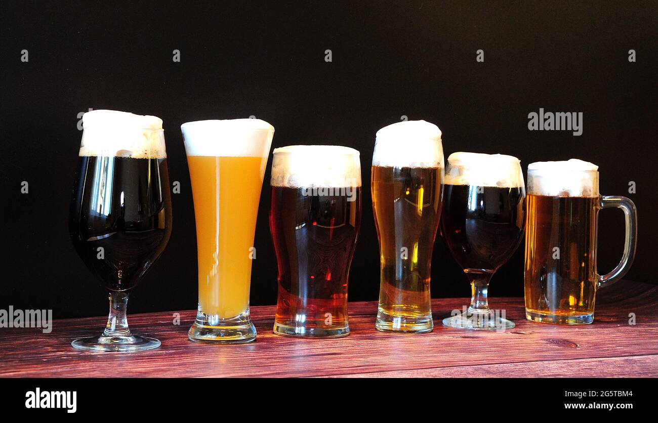 Six bières différentes dans six verres différents se tiennent dans une rangée sur une table en bois. Gros plan. Banque D'Images