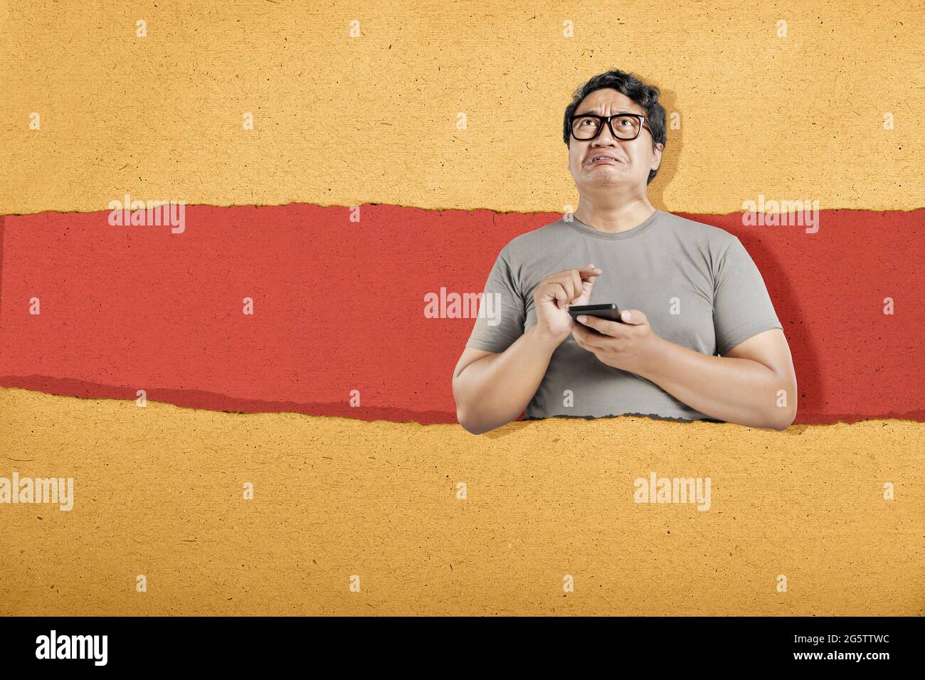 Homme asiatique en lunettes de vue avec expression malheureuse avec fond de papier déchiré Banque D'Images