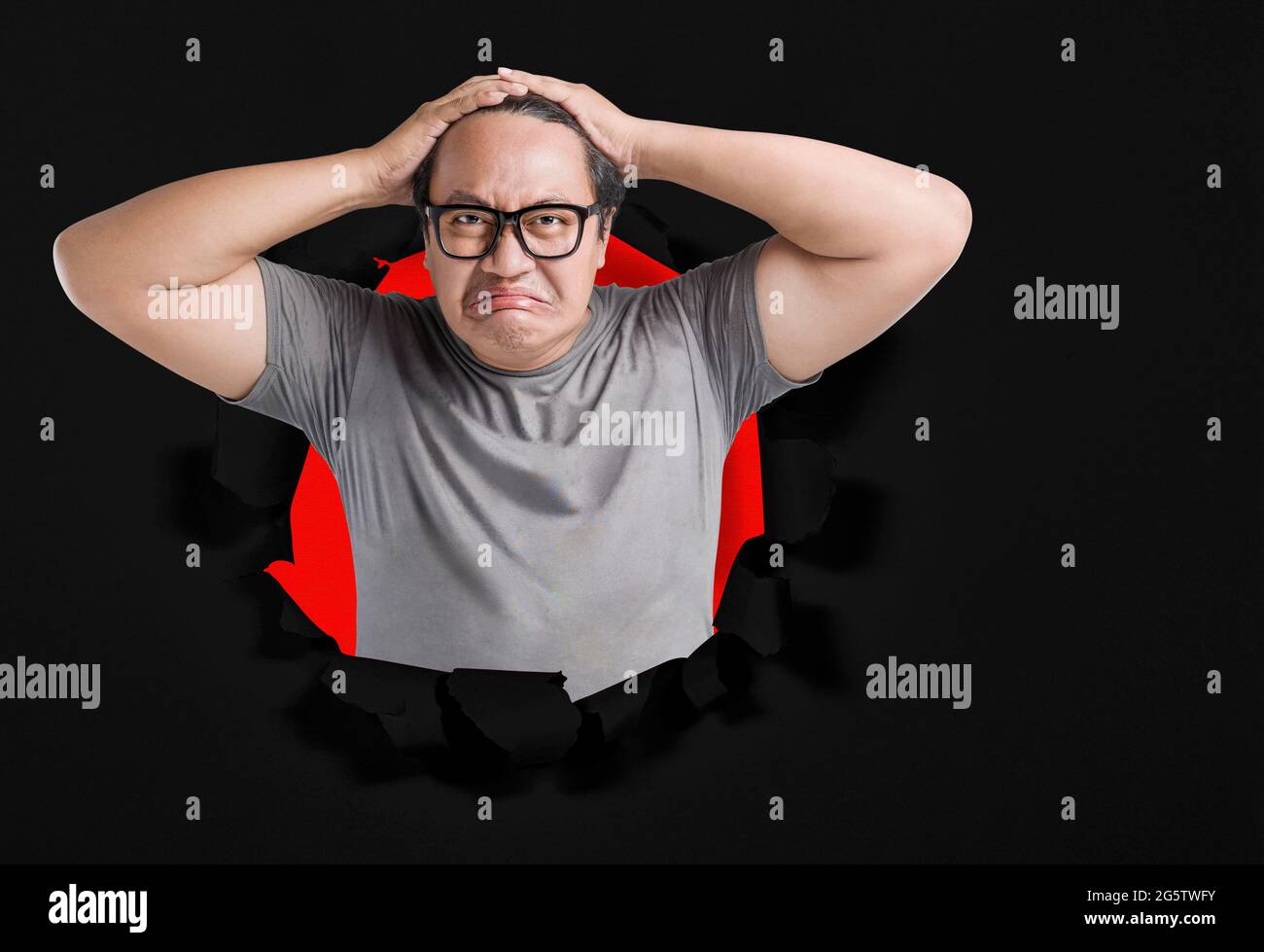 Homme asiatique en lunettes de vue avec expression malheureuse avec fond de papier déchiré Banque D'Images