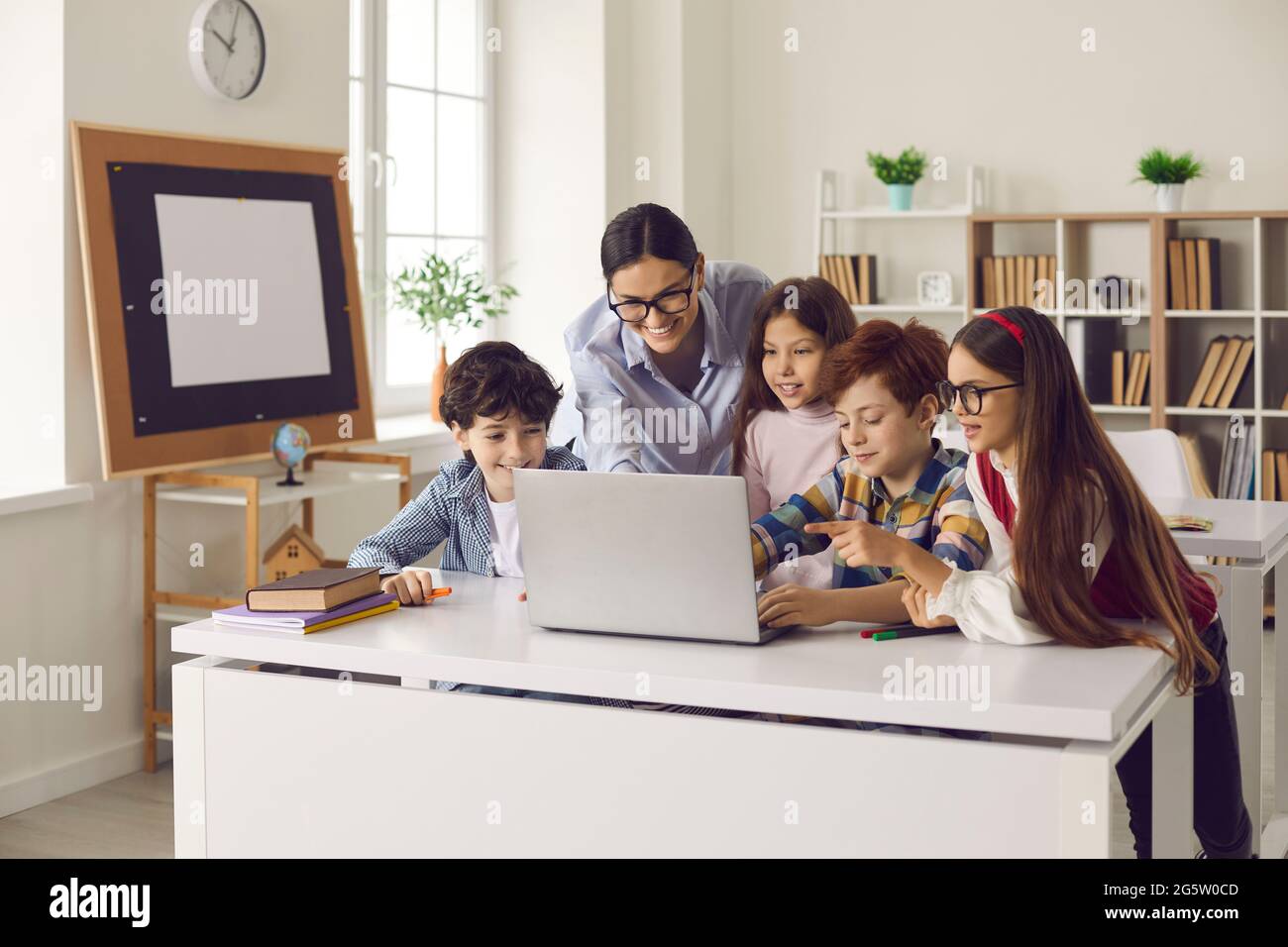 Les enfants des écoles primaires et les enseignantes en classe travaillent ensemble sur ordinateur portable. Banque D'Images