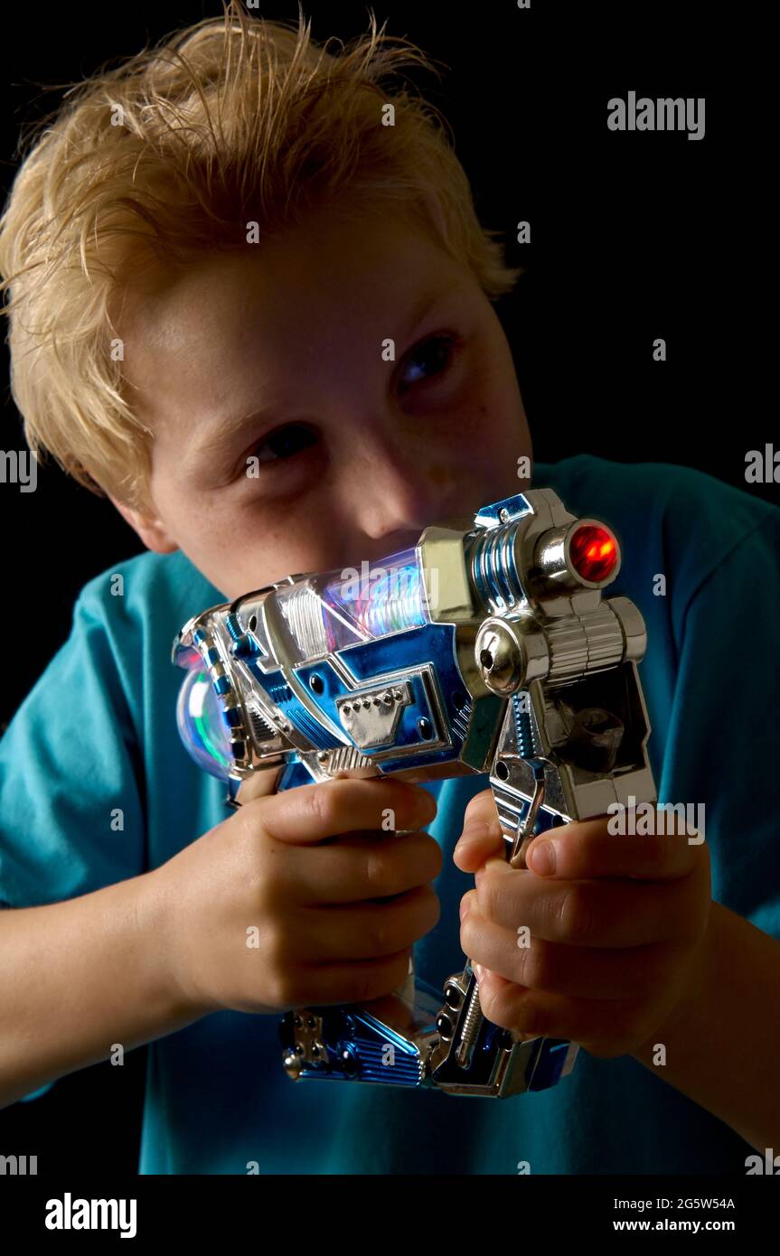 jeune garçon blond aux cheveux jouant avec un fusil laser en peluche dans l'obscurité Banque D'Images