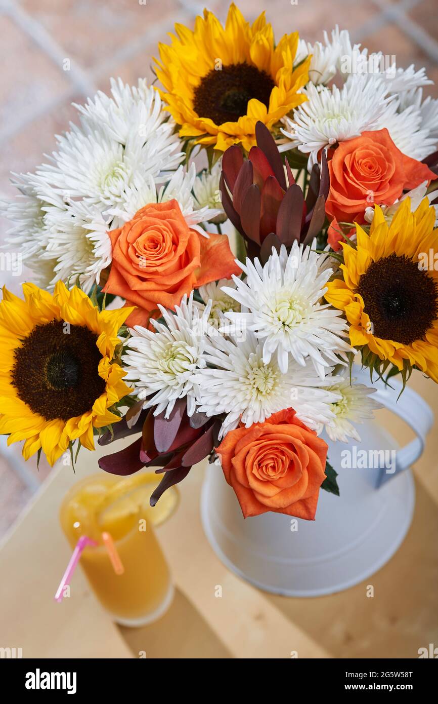 Bouquet de fleurs d'été mélangées dans une verseuse blanche sur une table basse à côté d'un verre de jus d'orange dans un cadre familial Banque D'Images