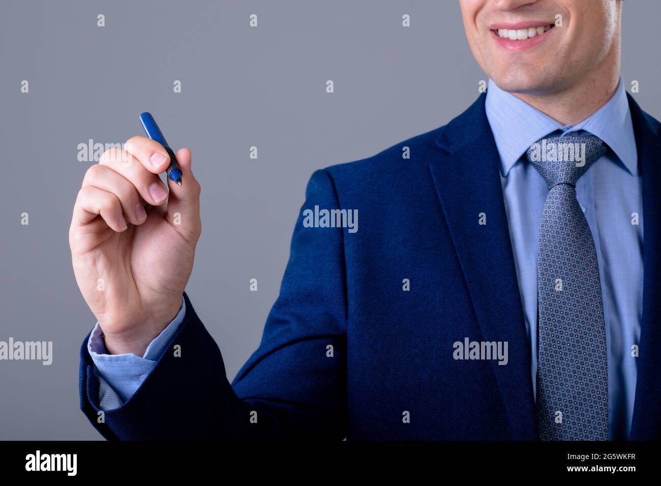 Homme d'affaires caucasien souriant tenant un stylo, isolé sur fond gris Banque D'Images