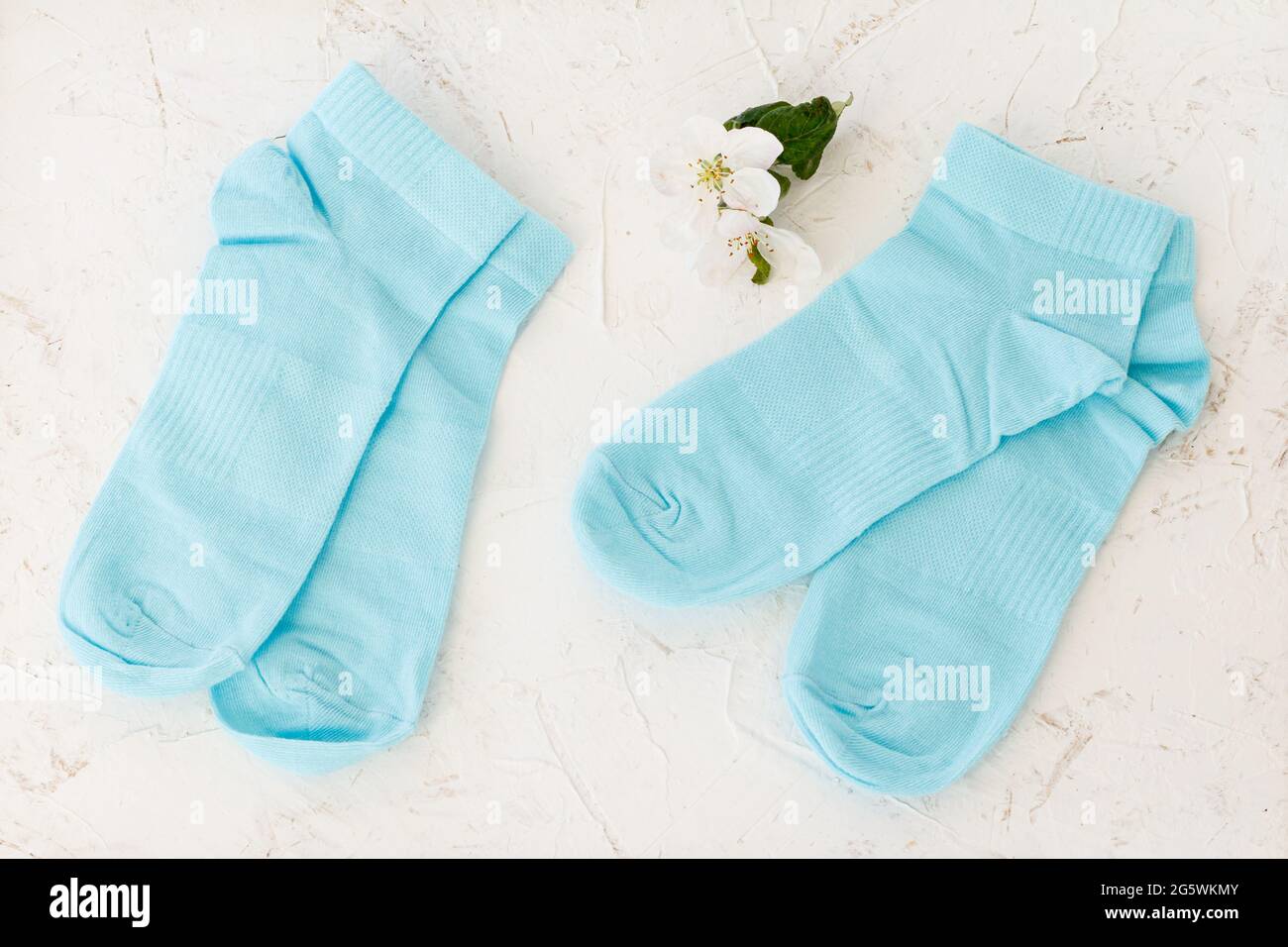 Deux paires de chaussettes bleues pour femmes et fleurs d'un pommier sur fond blanc structuré, vue du dessus. Banque D'Images