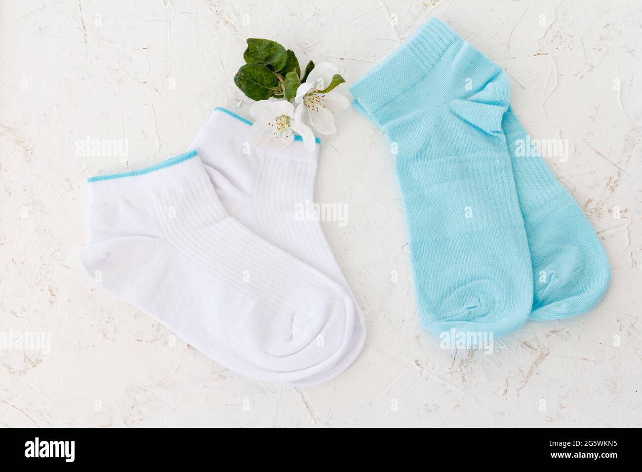 Deux paires de chaussettes pour femmes et fleurs d'un pommier sur fond blanc structuré, vue du dessus. Banque D'Images