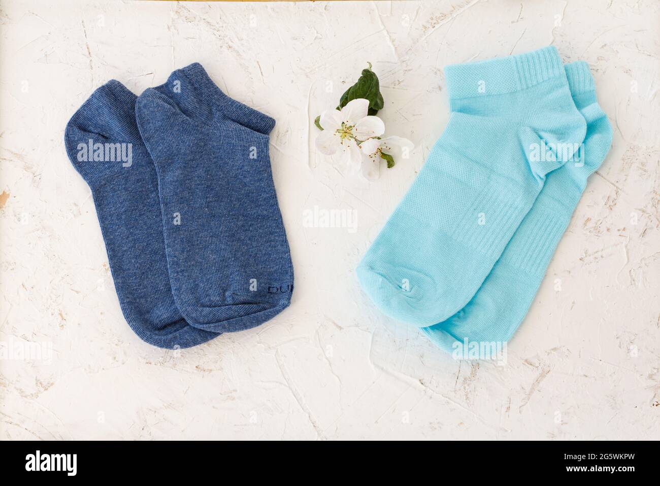 Deux paires de chaussettes bleues pour femmes et fleurs d'un pommier sur fond blanc structuré, vue du dessus. Banque D'Images