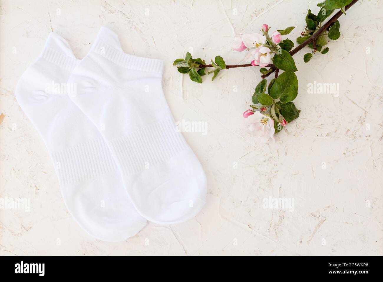 Paire de chaussettes blanches pour femmes et fleurs d'un pommier sur fond blanc structuré, vue du dessus. Banque D'Images