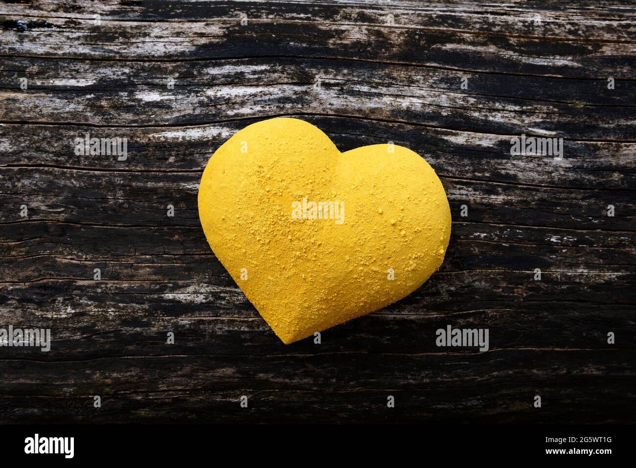 forme de coeur en 3 dimensions peinte en jaune, et parsemée de pigment sec, sur fond de bois abîmé. Banque D'Images