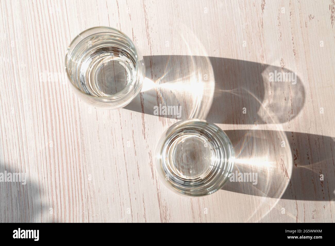 Deux verres d'eau sur fond de bois blanc sous le soleil direct brille. Vue de dessus des verres d'eau. Effet de réflexion caustique. Banque D'Images