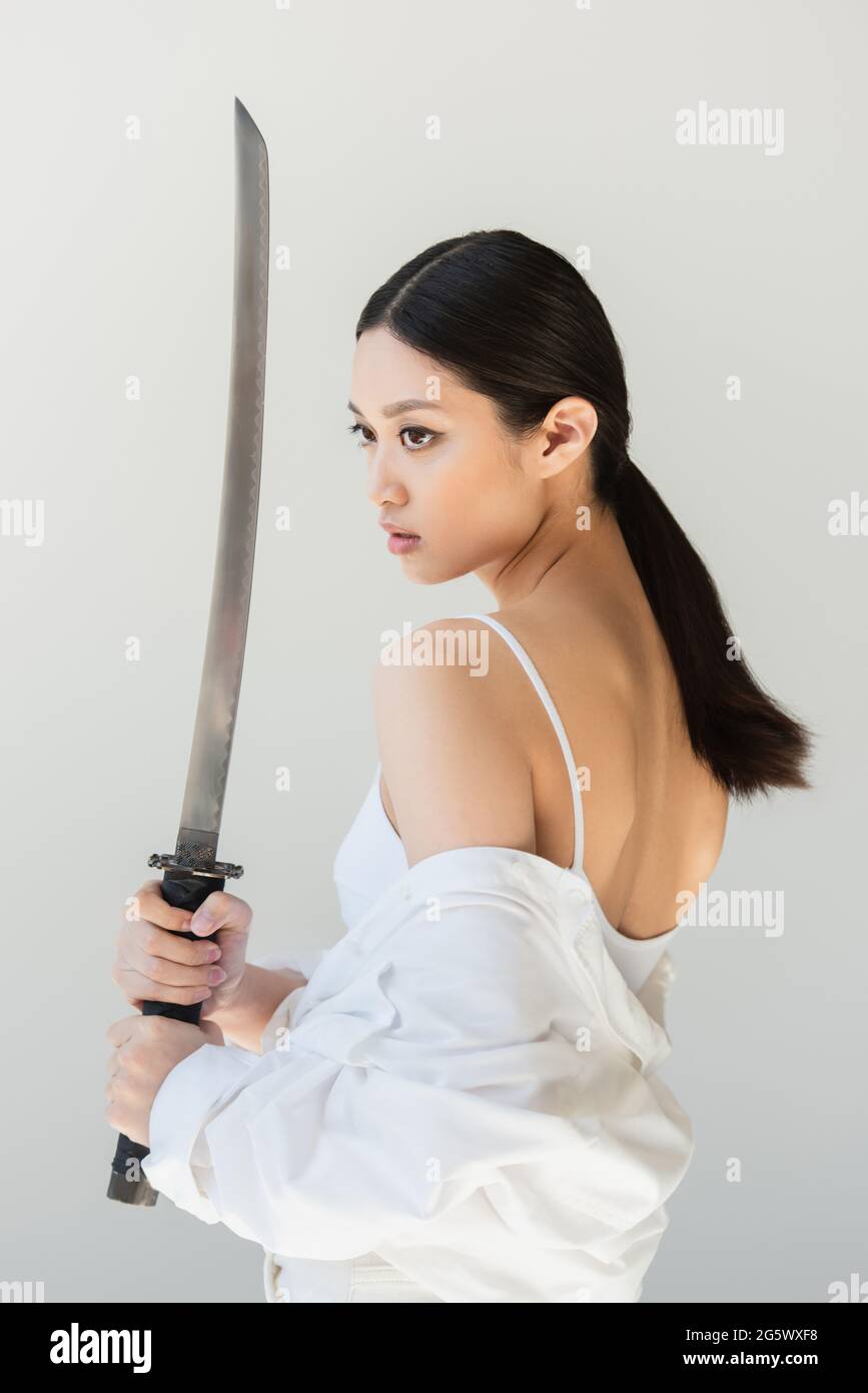 Jolie femme japonaise tenant une épée wakizashi isolée sur gris Banque D'Images