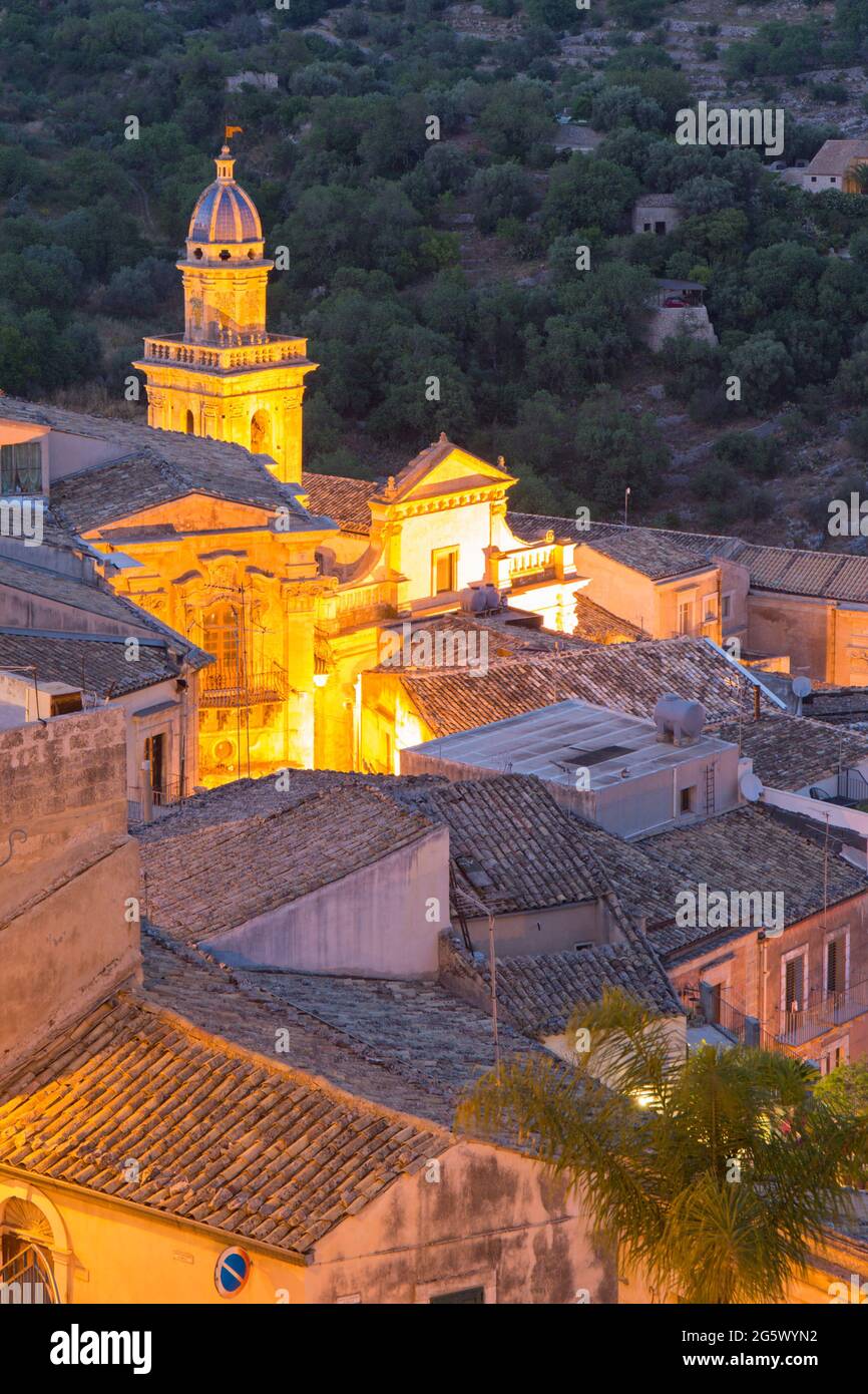 Ragusa, Sicile, Italie. Vue sur les toits carrelés au crépuscule, la façade et le clocher de l'église de Santa Maria dell'Itria sont illuminés. Banque D'Images