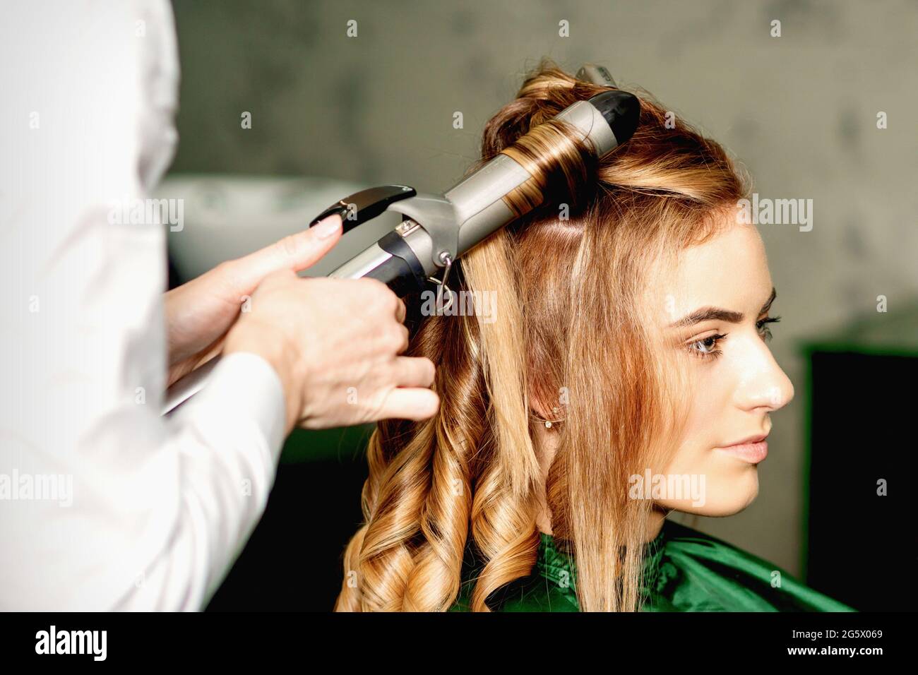 Coiffeur à l'aide de pinces à boucler cheveux longs bruns sur la jeune  fille caucasienne dans un salon de beauté Photo Stock - Alamy
