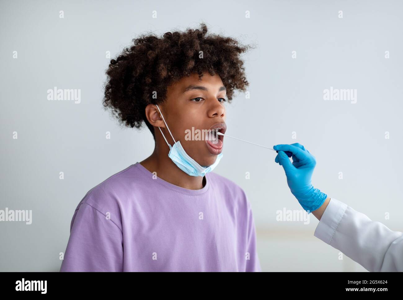 Médecin effectuant un test PCR du coronavirus oral pour un adolescent noir à la clinique. Concept de prévention des maladies infectieuses Banque D'Images