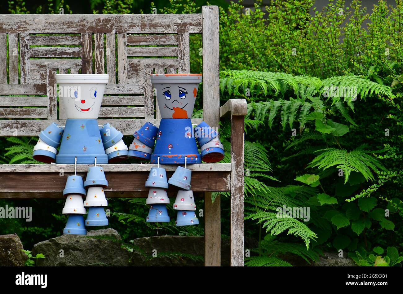 Assis sur un banc de jardin en bois 2 pots de fleurs décorés et peints bleu clair et bleu foncé sont vus dans un jardin dans le nord du Somerset au Royaume-Uni. Banque D'Images