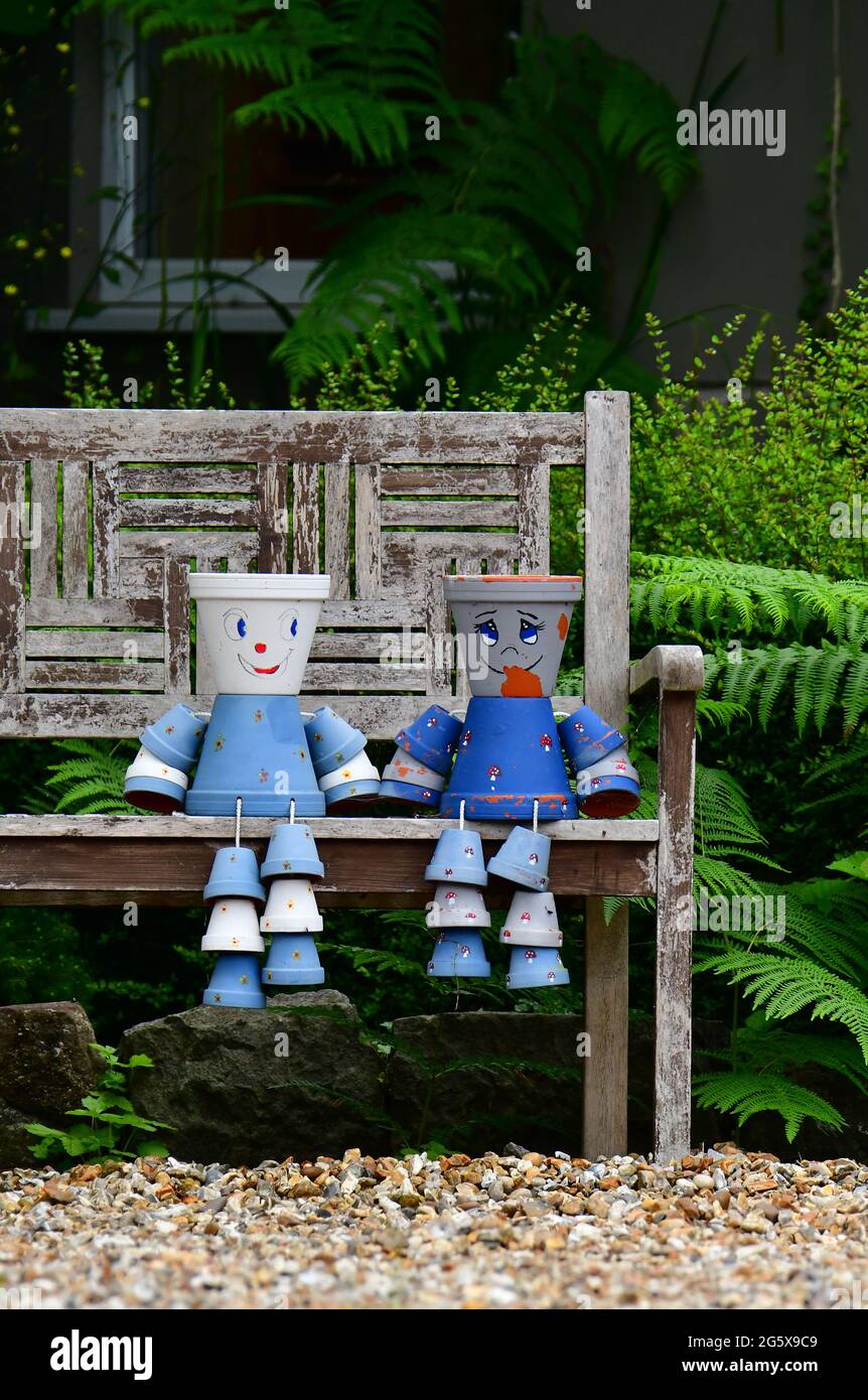 Assis sur un banc de jardin en bois 2 pots de fleurs décorés et peints bleu clair et bleu foncé sont vus dans un jardin dans le nord du Somerset au Royaume-Uni. Banque D'Images