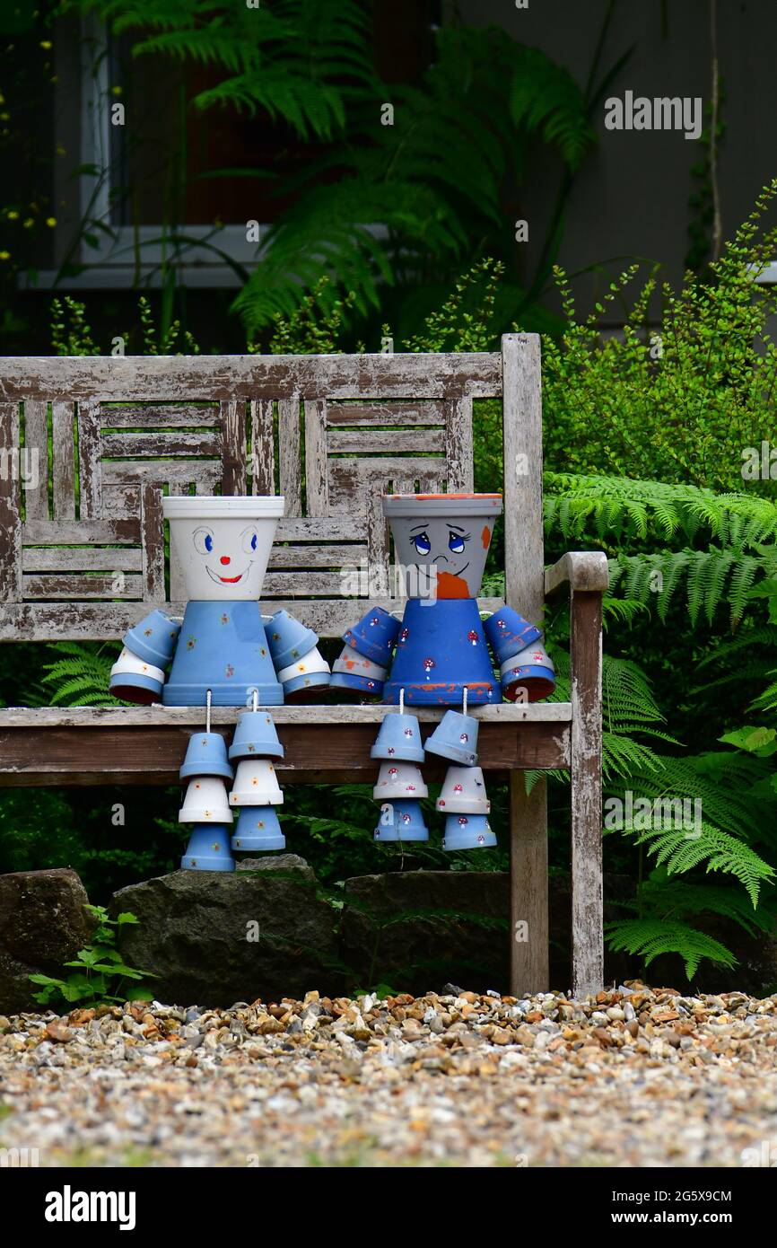 Assis sur un banc de jardin en bois 2 pots de fleurs décorés et peints bleu clair et bleu foncé sont vus dans un jardin dans le nord du Somerset au Royaume-Uni. Banque D'Images