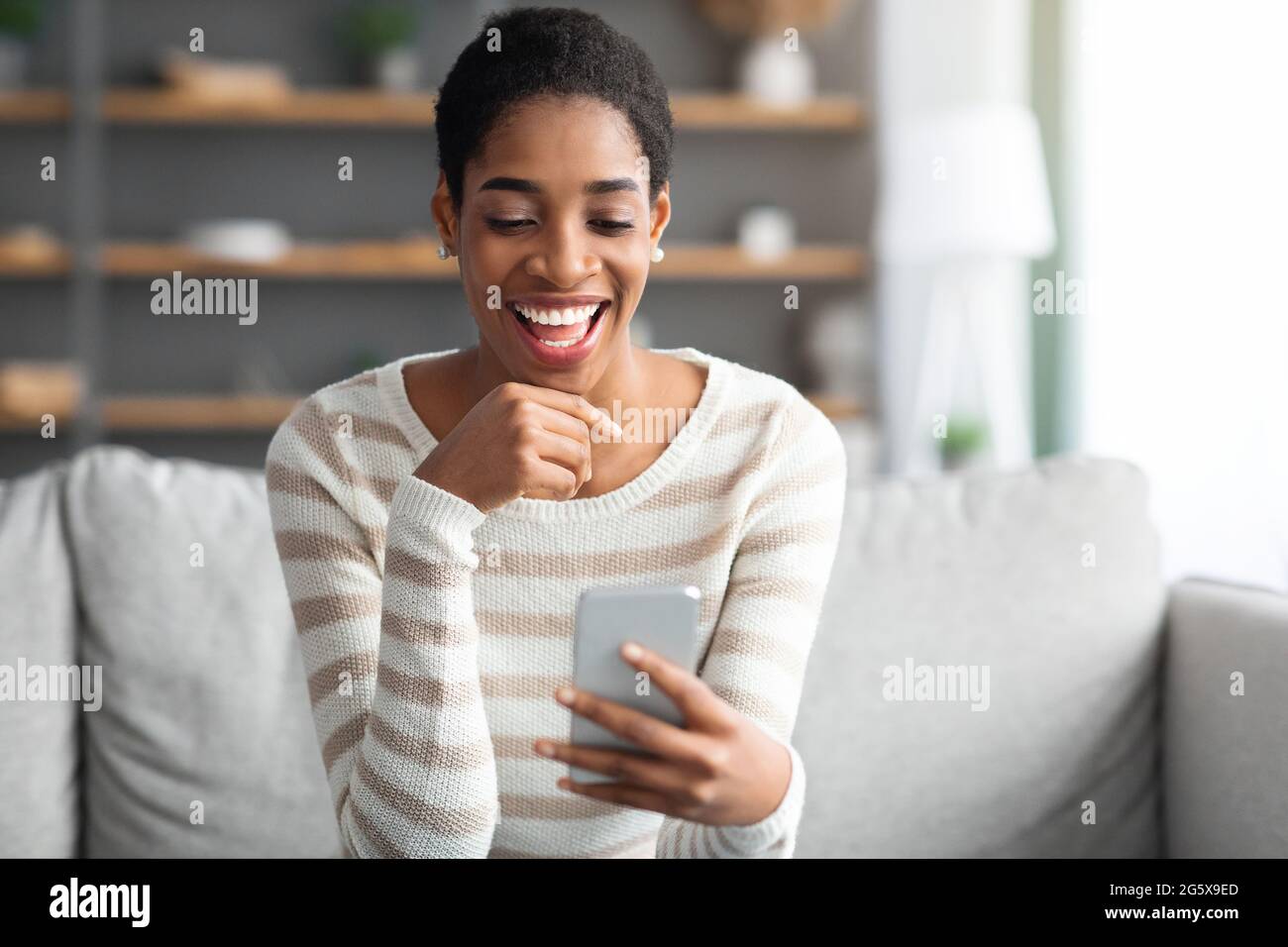 Application de datation en ligne Jeune femme seule noire utilisant un smartphone à la maison Banque D'Images