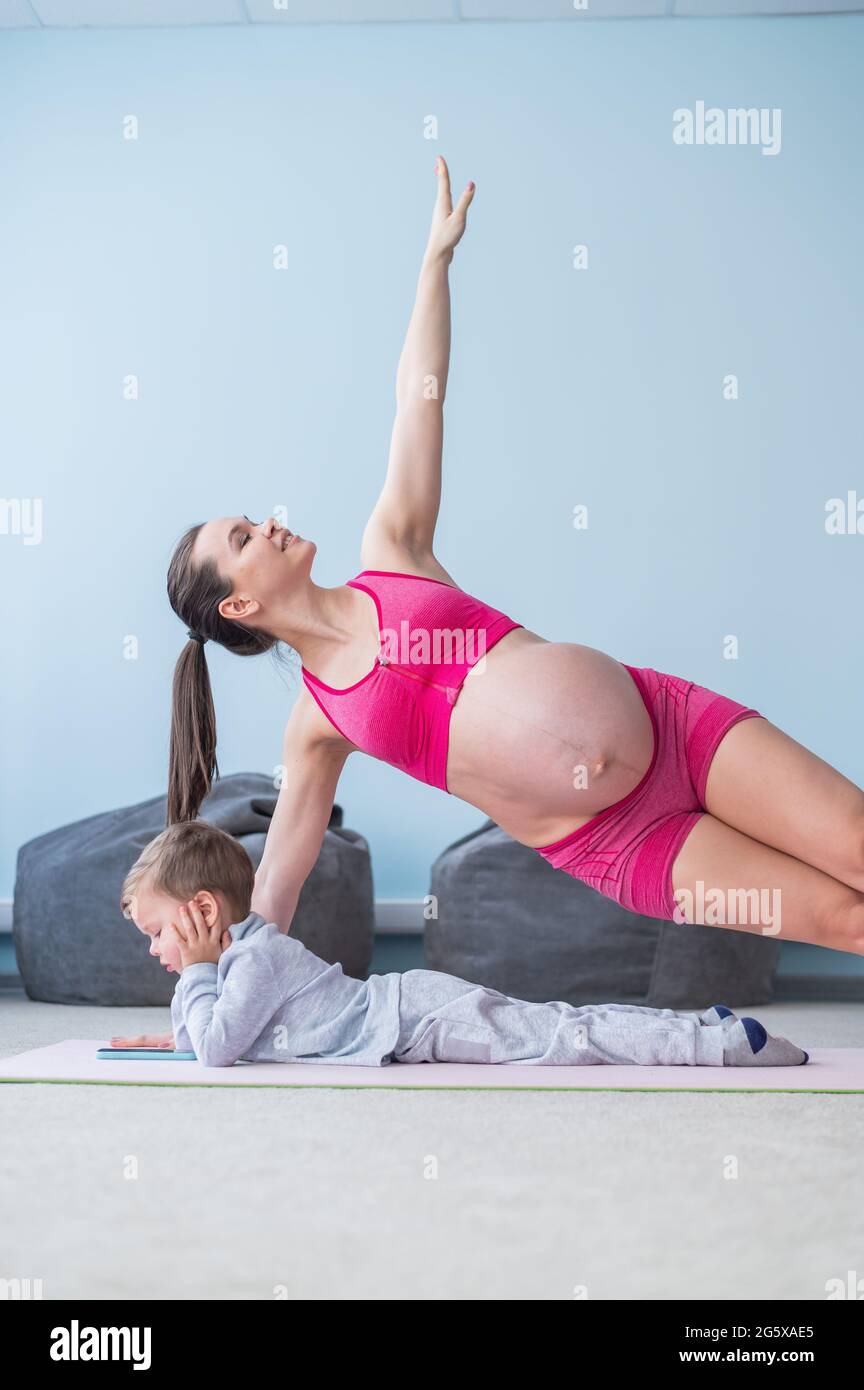 Une femme enceinte en vetements de sport fait de la gymnastique pendant que son fils joue dans le mobile. Fille sur le yoga avec son enfant. Fitness maman et bebe Photo Stock
