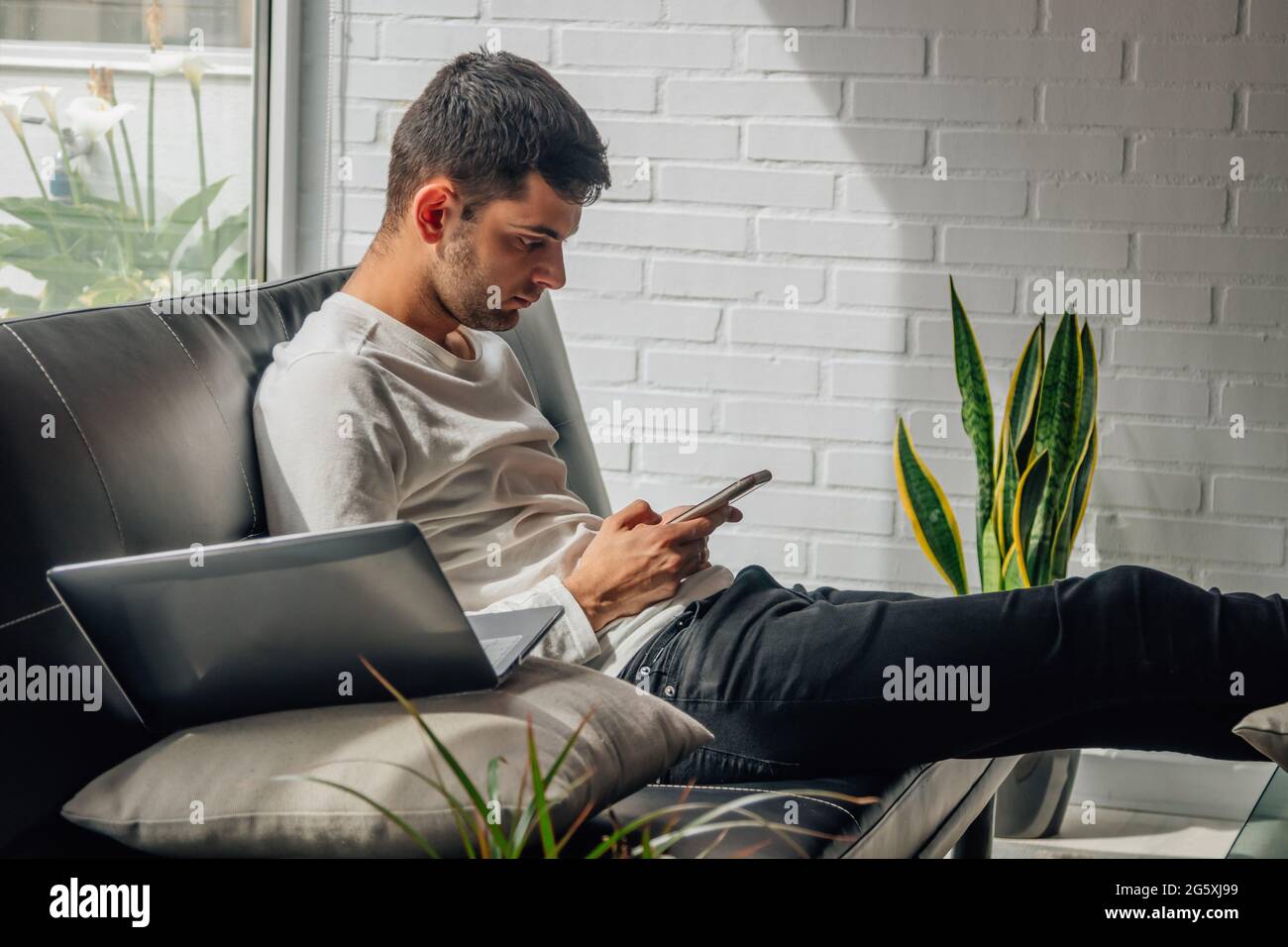 jeune homme avec téléphone portable à la maison assis sur le canapé Banque D'Images