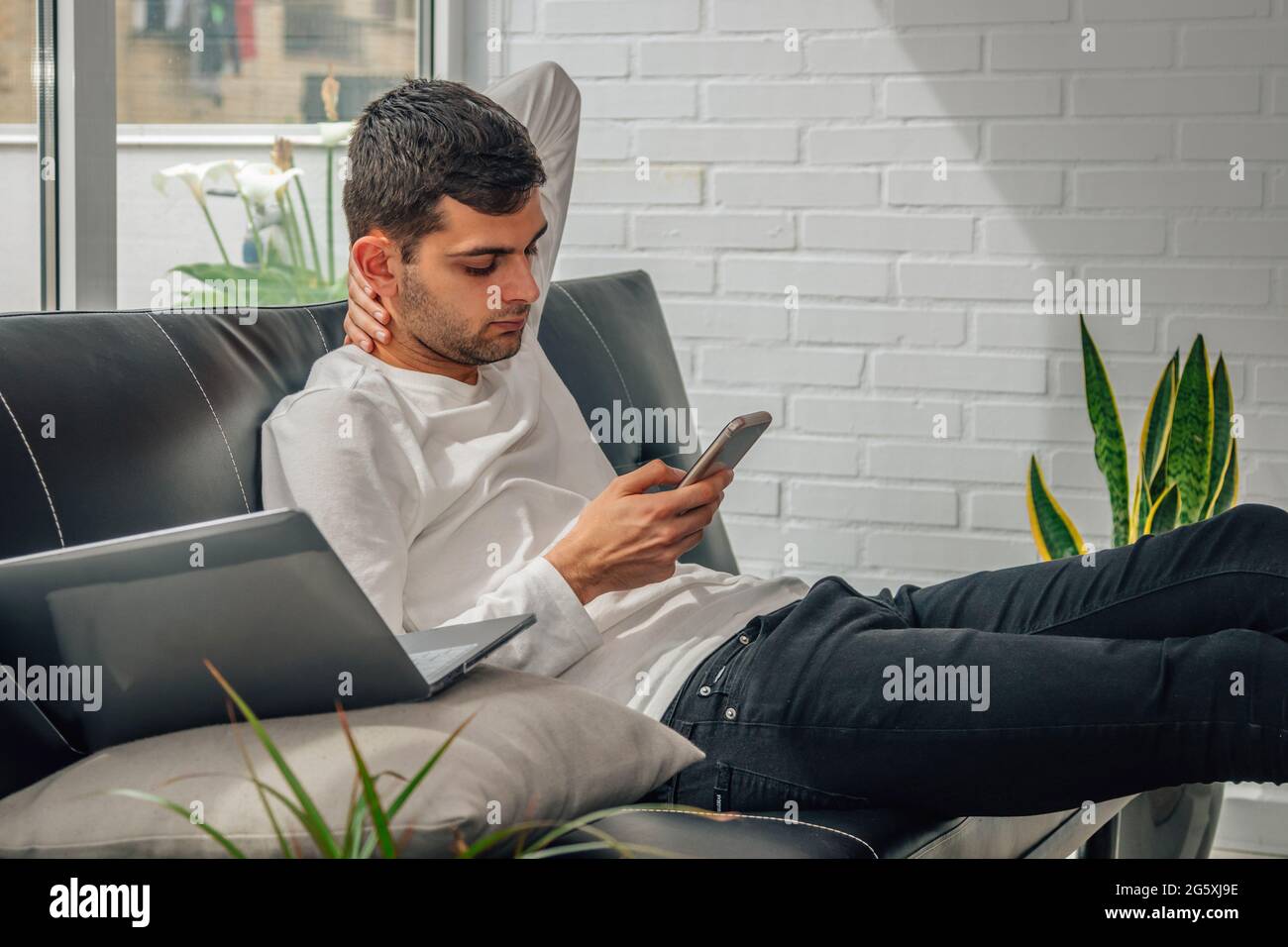 jeune homme avec téléphone portable à la maison assis sur le canapé Banque D'Images