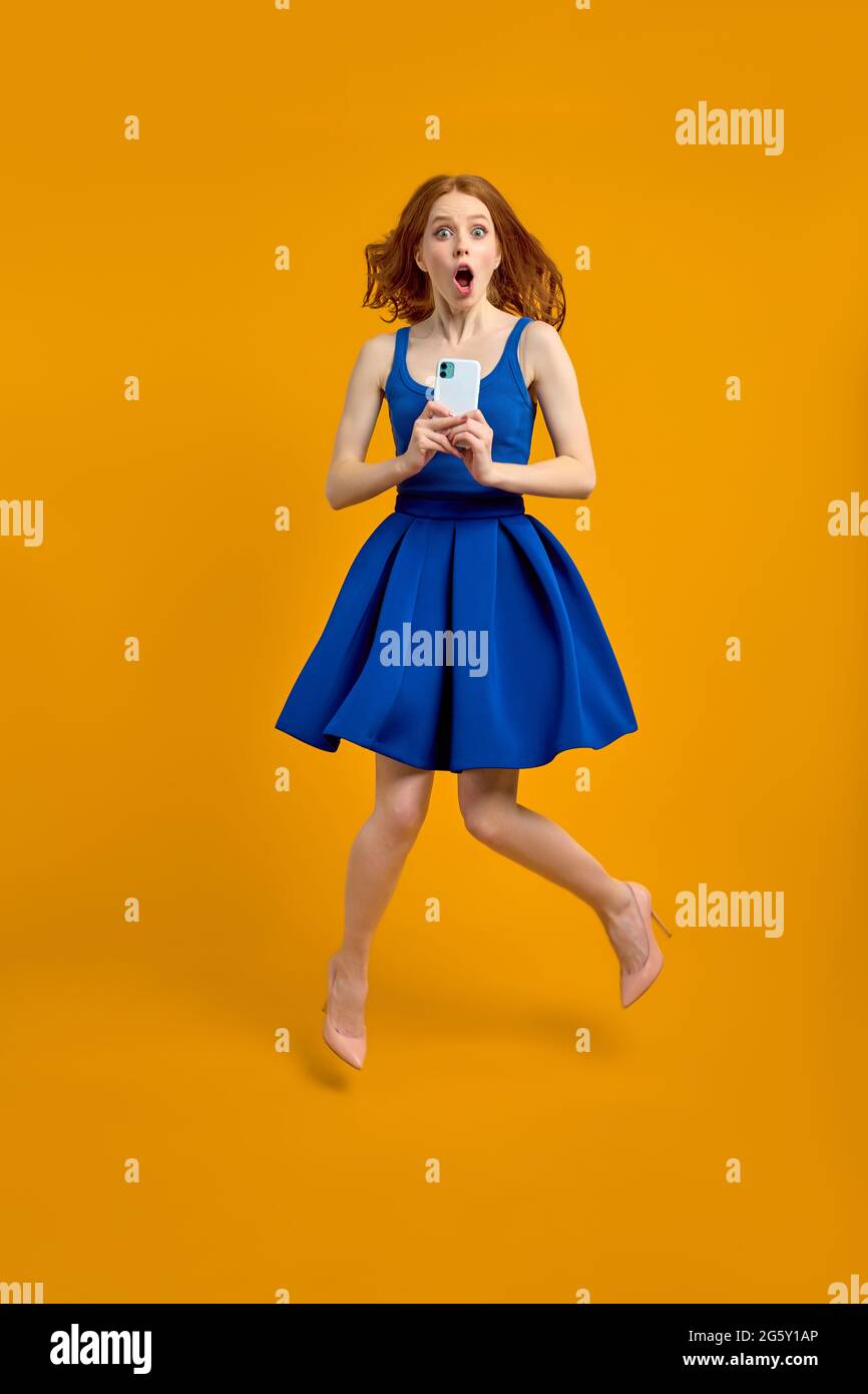 Pleine longueur profil photo de la dame choc redhead saut haut tenant téléphone, lire le blog de choc commentaires porter printemps été bleu robe isolé y Banque D'Images