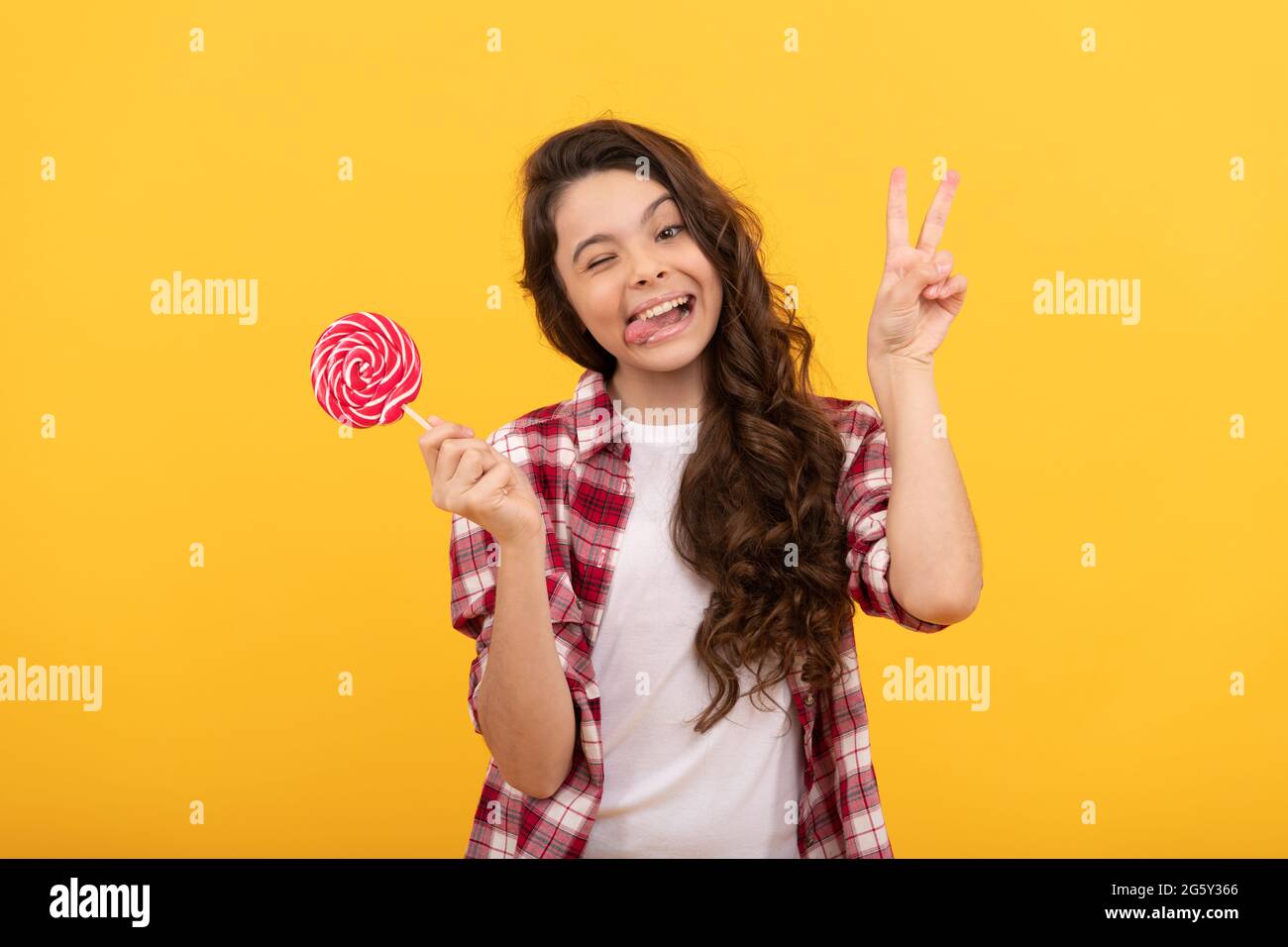 drôle de fille de l'adolescence tenir lollipop caramel bonbon sur fond jaune montrer le geste de paix, boutique de caramel. Banque D'Images