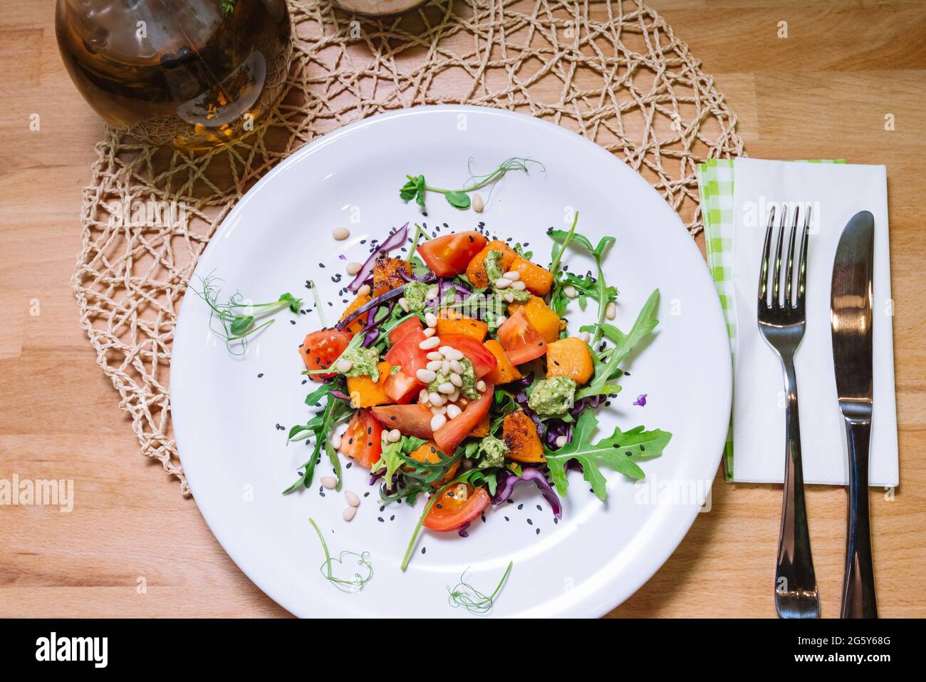 Salade chaude avec citrouille, tomates, arugula, sauce pesto avec pignons de pin et graines de sésame noir sur la plaque blanche vue du dessus Banque D'Images