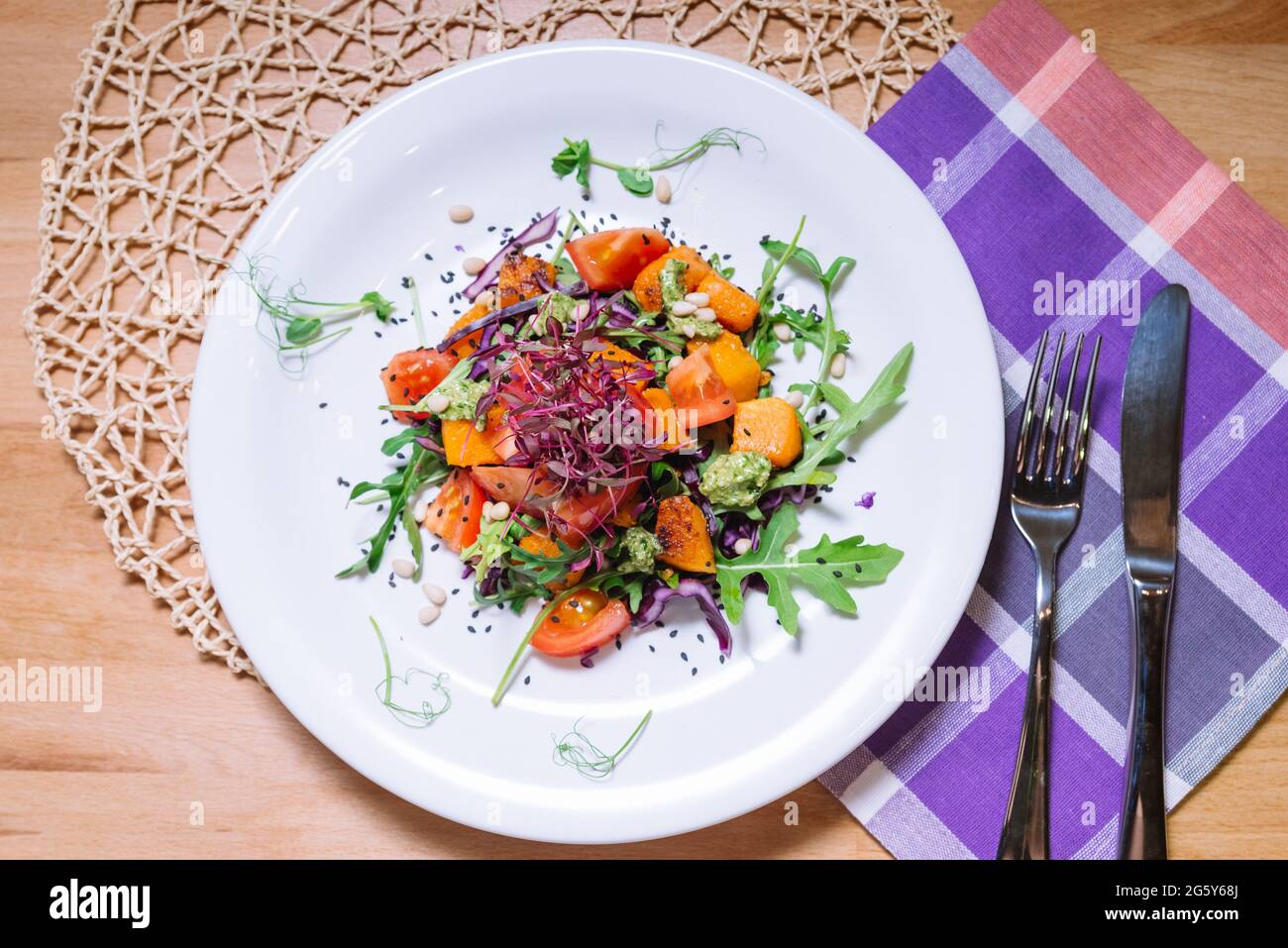 Salade chaude avec citrouille, tomates, arugula, sauce pesto avec pignons de pin et graines de sésame noir sur la plaque blanche vue du dessus Banque D'Images
