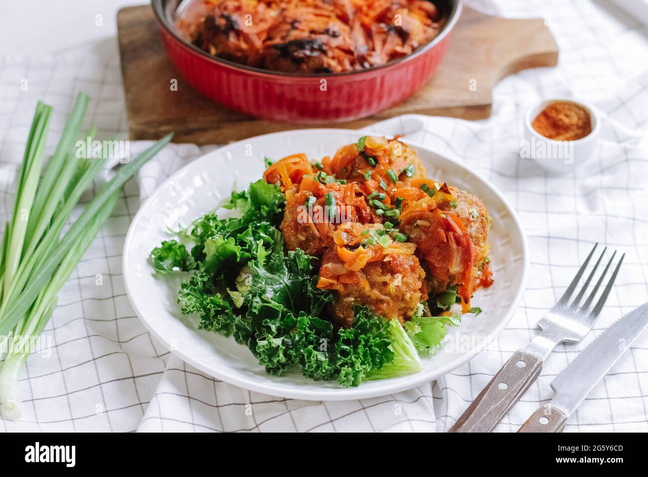 portion de boulettes de viande cuites au four avec légumes et feuilles de salade sur une assiette blanche. repas maison. parsemé de scallion. intérieur de la table de cuisine maison. Banque D'Images