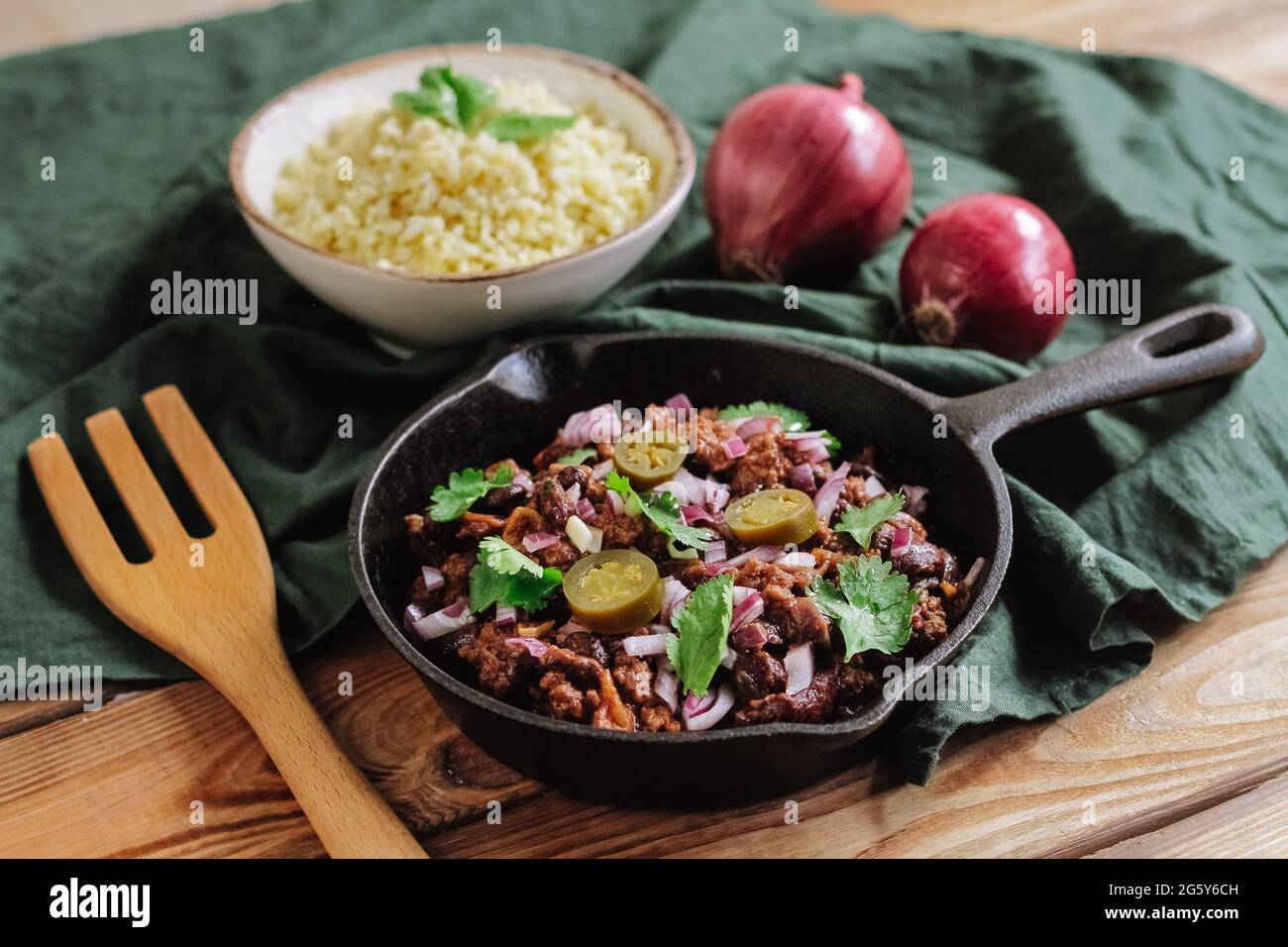 Petite poêle en fer noir avec repas chaud maison de viande de bœuf hachée, pepperoni et oignon rouge parsemé de feuilles d'herbes fraîches. Et grits (bulgur) Banque D'Images