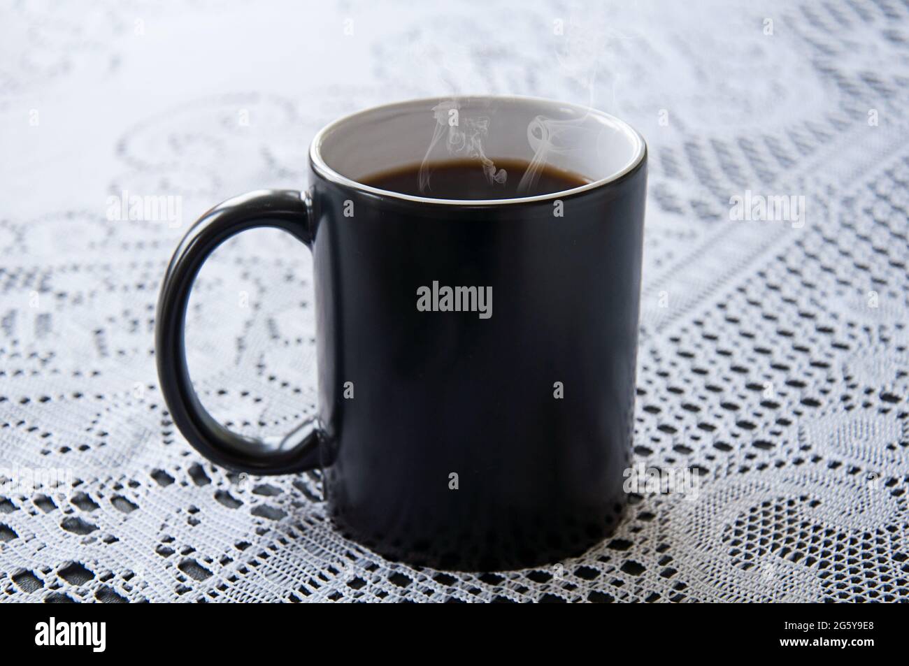 Une tasse de café chaud à la vapeur dans une tasse de café noir sur une nappe en dentelle blanche. Boisson classique encore plus vivant avec l'espace de copie sur la tasse à café noire. Banque D'Images