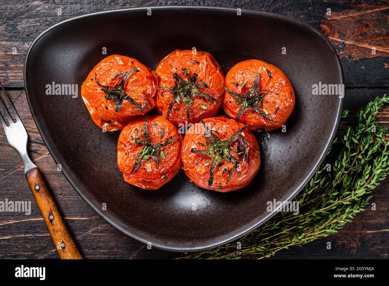 Faire cuire au four des tomates cerises rôties avec du thym et de l'ail  dans une assiette. Arrière-plan en bois sombre. Vue de dessus Photo Stock -  Alamy