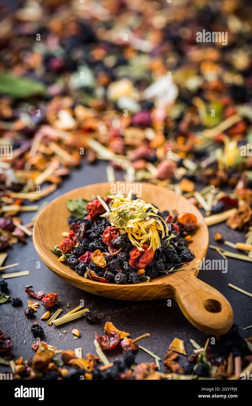 Feuilles de thé séchées, fruits et baies dans un bol sur une table rustique en bois Banque D'Images