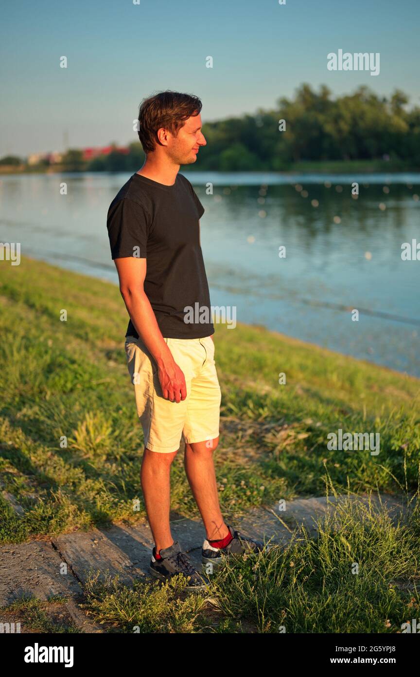 Portrait d'un homme mûr debout sur la rive du lac pendant le coucher du soleil Banque D'Images