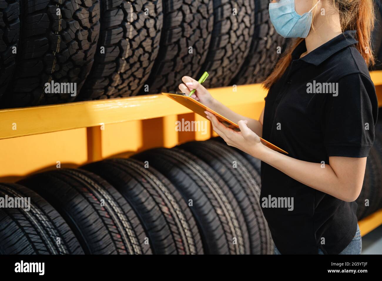 Gros plan la travailleuse porte un masque pour empêcher la propagation du virus corona ou COVID-19 en vérifiant le stock de pneus de voiture à l'entrepôt et en écrivant certains non Banque D'Images