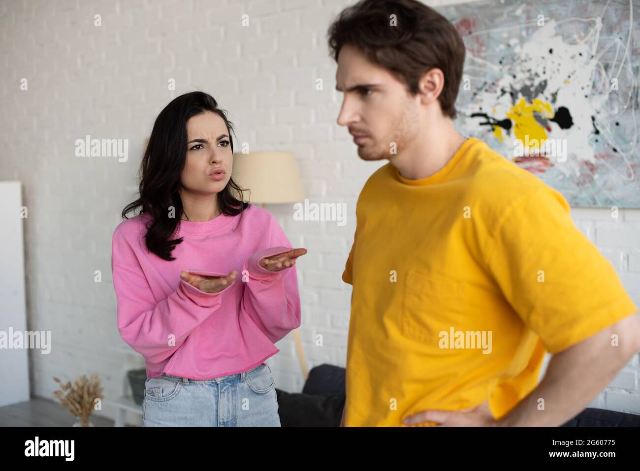une jeune femme en colère criait avec des mains tendues près d'un petit ami avec la main sur la posture de la hanche dans le salon Banque D'Images