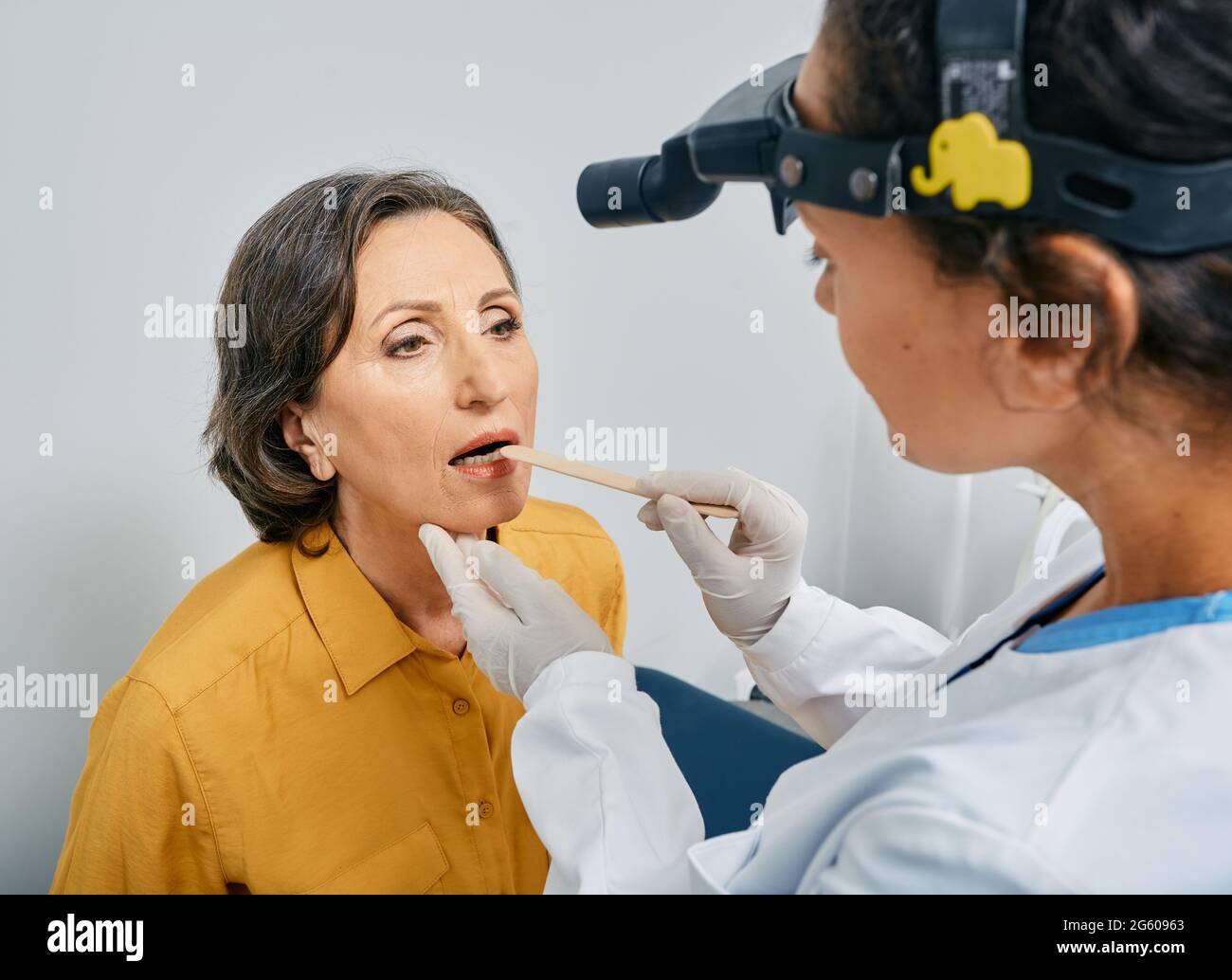 Otolaryngologiste utilisant la spatule d'inspection pour examiner la gorge de la femme mature. Une patiente âgée ouvre la bouche pendant le contrôle de la gorge Banque D'Images