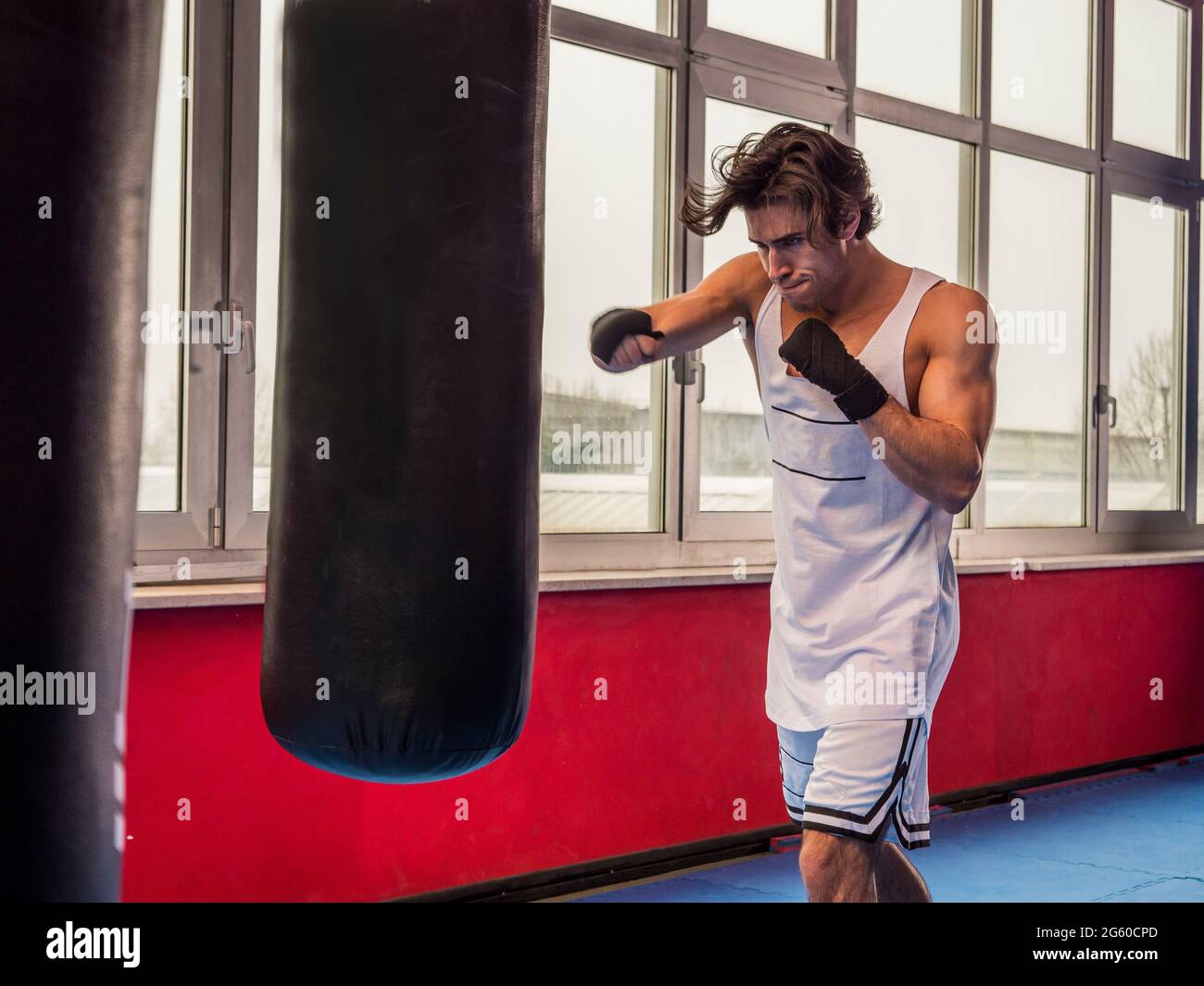 Musculent sportive homme entraînement avec sac de poinçonnage pendant la boxe Banque D'Images