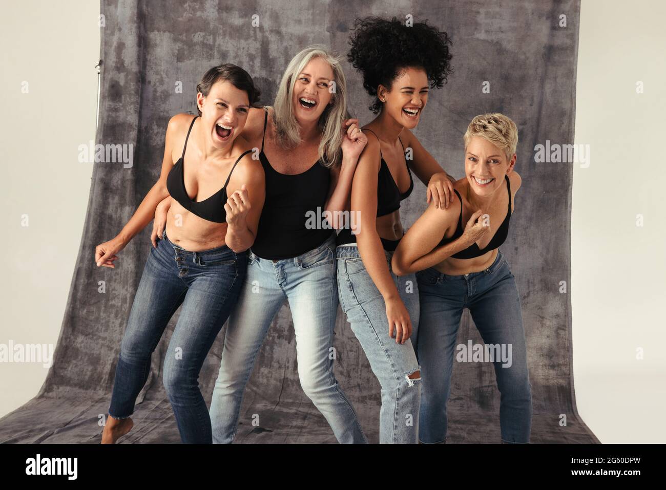 Groupe de femmes diverses s'amusant en portant des jeans et des soutiens-gorge. Quatre femmes positives de corps de différents âges souriant gaiement et célébrant leur na Banque D'Images