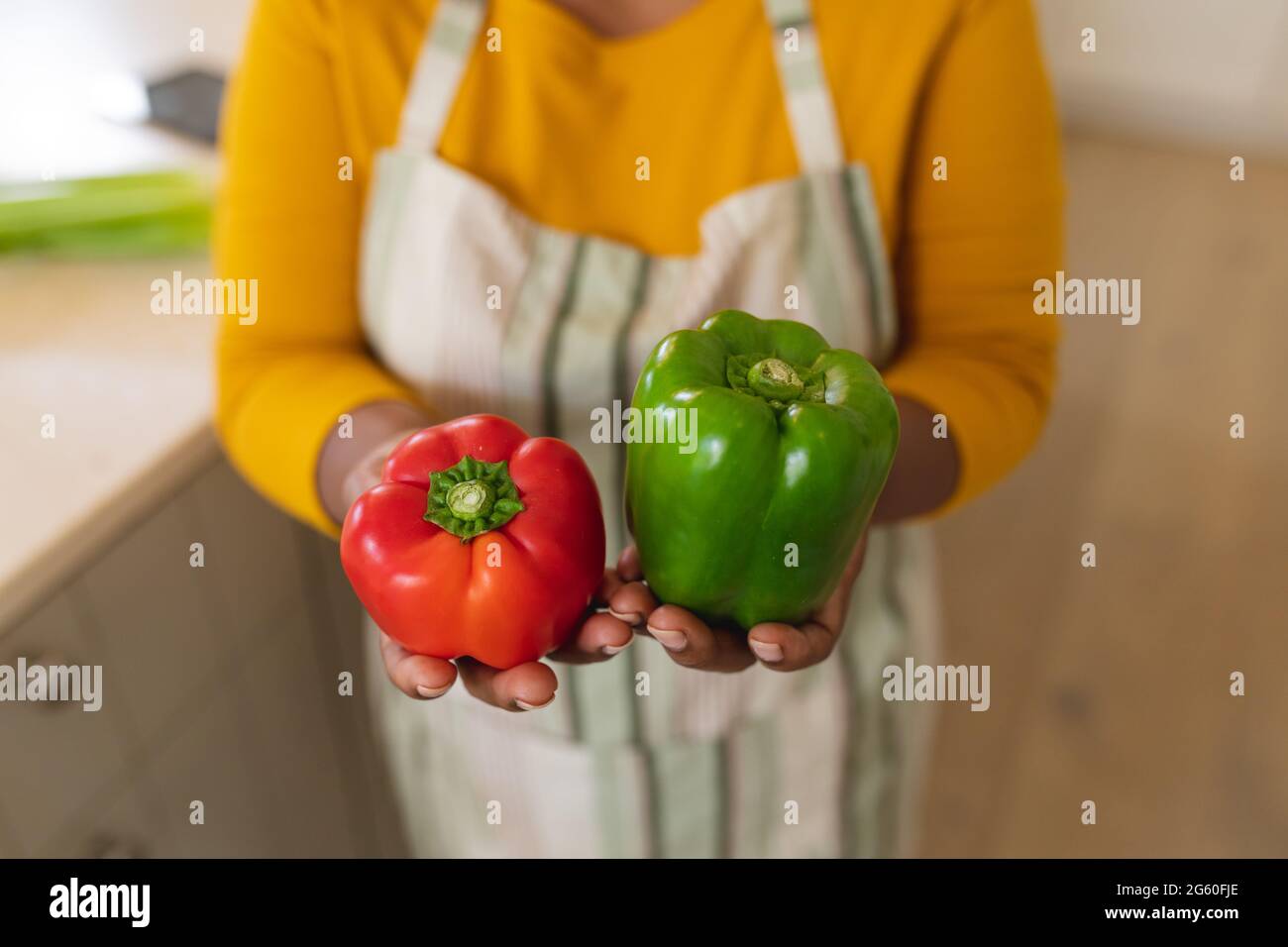 Vue en coupe du milieu de la femme afro-américaine senior tenant des poivrons dans la cuisine Banque D'Images