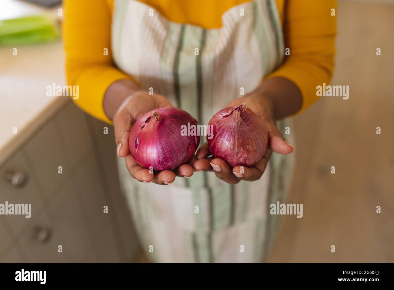 Vue en coupe du milieu de la femme afro-américaine senior tenant des oignons dans la cuisine Banque D'Images