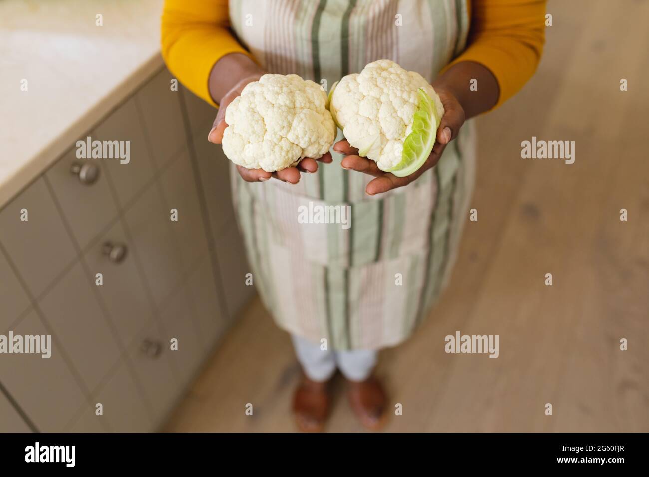 Vue de la section médiane de la femme afro-américaine senior tenant des choux-fleurs dans la cuisine Banque D'Images