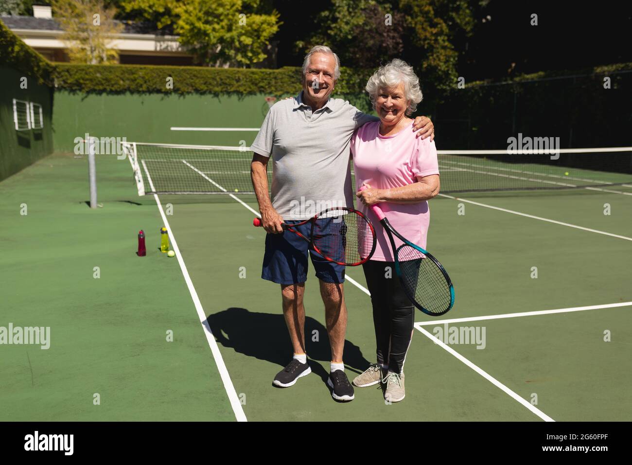 Portrait d'un couple caucasien âgé regardant l'appareil photo et souriant sur un court de tennis Banque D'Images